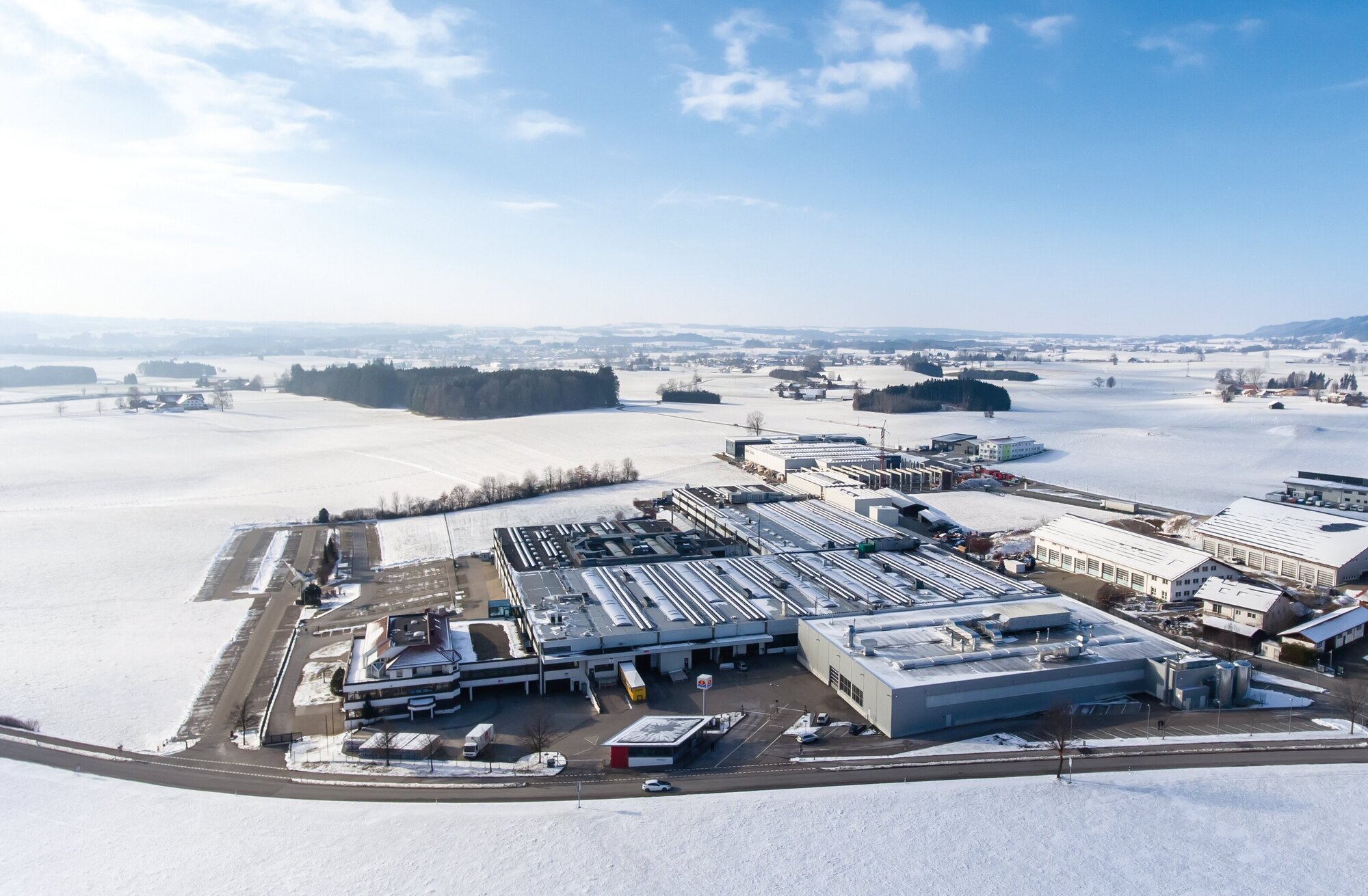 Vogelperspektive auf eine schneebedeckte Fabrik, die in einer winterlichen Landschaft eingebettet ist